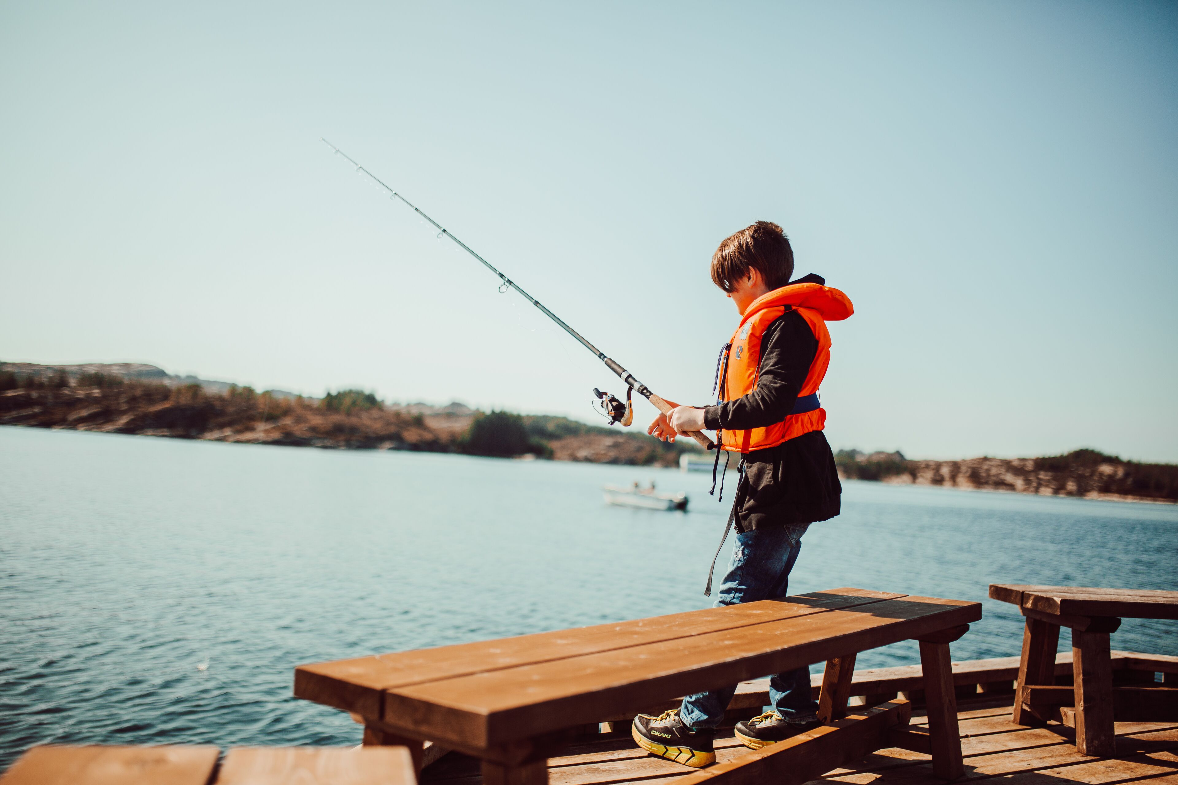 A person fishing by a wooden dock with a clear view of the water and distant land.