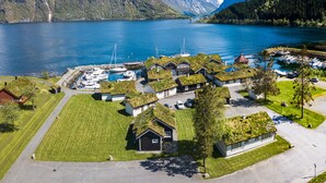 Uma vila costeira com casas de telhados verdes, uma marina com barcos e montanhas nevadas ao fundo.