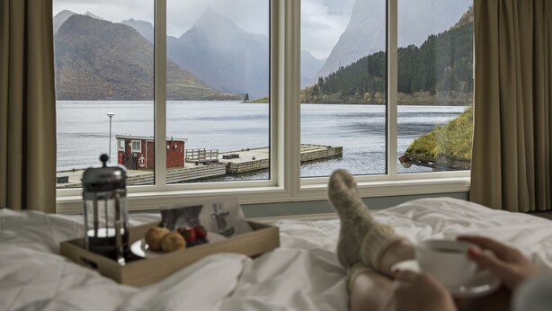 Cama com vista para um lago, montanhas e um píer.