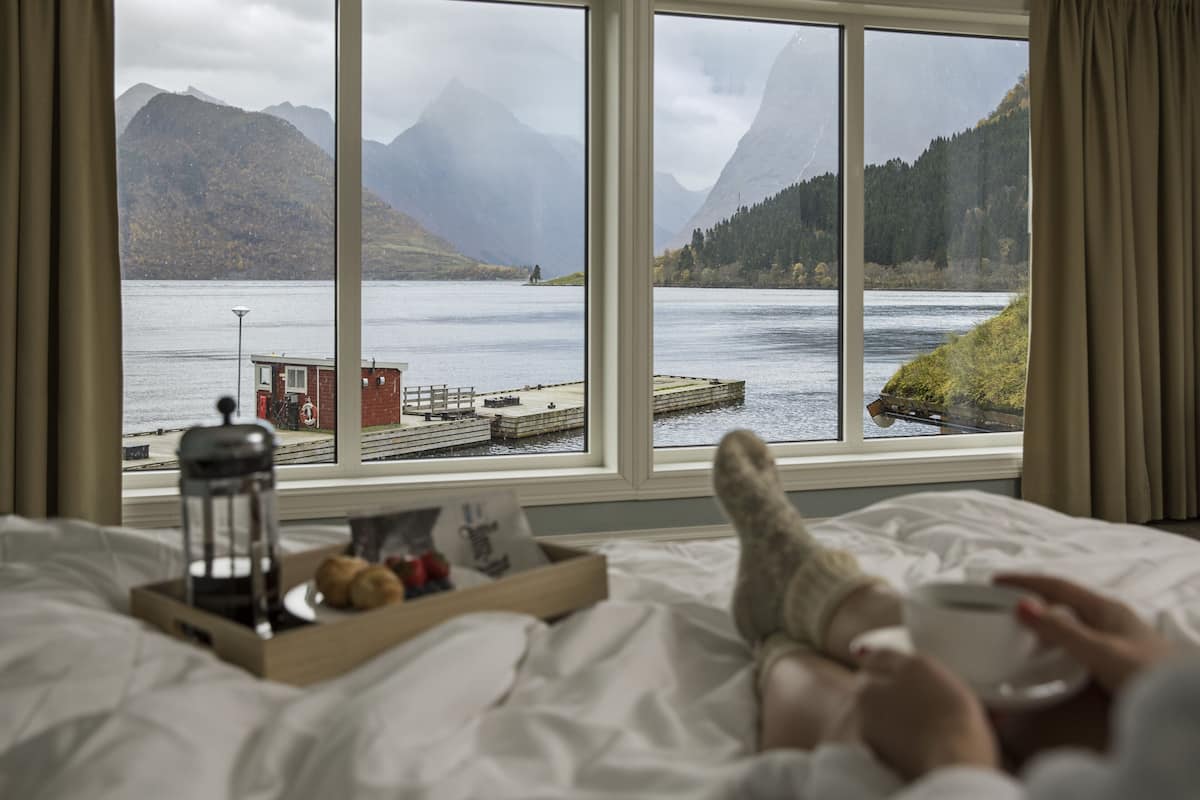 A bed with a view of a lake, mountains, and a dock.