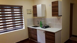 Una pequeña cocina con ventana, un fregadero, una botella verde y una cafetera.