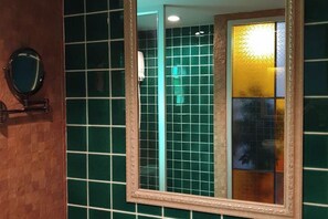 A bathroom with green tiles, a mirror, and a glass partition.