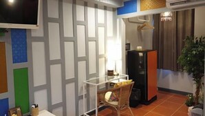 A room with a TV mounted on the wall, a table with chairs, a refrigerator, and a potted plant. - Baan Baimai Boutique Room (Ayutthaya)