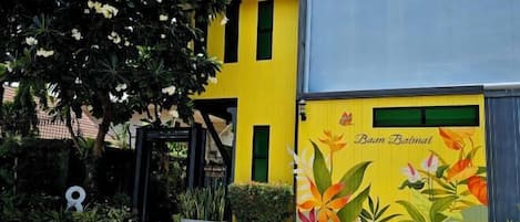 A building with a yellow and blue facade, a mural with floral designs, and a black gate.