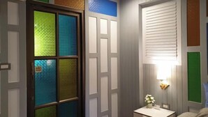A room with a frosted glass door, a bedside table with a lamp, and a window with blinds. - Baan Baimai Boutique Room (Ayutthaya)