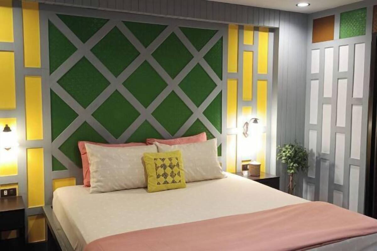Un lit bien fait, avec des oreillers, une table de chevet avec une lampe et un mur orné d’un motif géométrique.