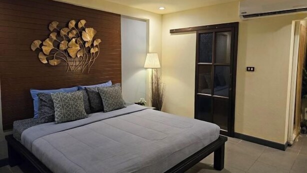 A bedroom with a bed, a wall-mounted artwork, a nightstand, and a door with a sliding mechanism. - Baan Baimai Boutique Room (Ayutthaya)
