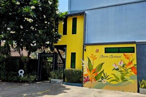 Un edificio con fachada amarilla y azul, un mural con diseños florales y una reja negra.