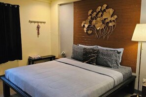 A bedroom with a bed, a wall-mounted decoration, a bedside table, and a lamp.