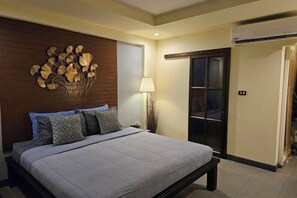 A bedroom with a bed, a wall-mounted artwork, a nightstand, and a door with a frosted glass panel. - Baan Baimai Boutique Room (Ayutthaya)