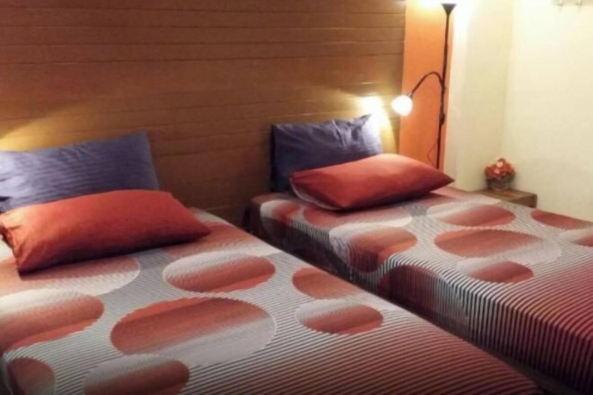 Une chambre avec deux lits, chacun recouvert d’une couvre-lit à motifs et agrémenté d’oreillers, un mur en briques, une table de chevet avec une lampe et une petite table sur laquelle est posé un vase.
