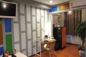 Habitación con televisor montado en la pared, una mesita con una silla, refrigerador y una planta en maceta.