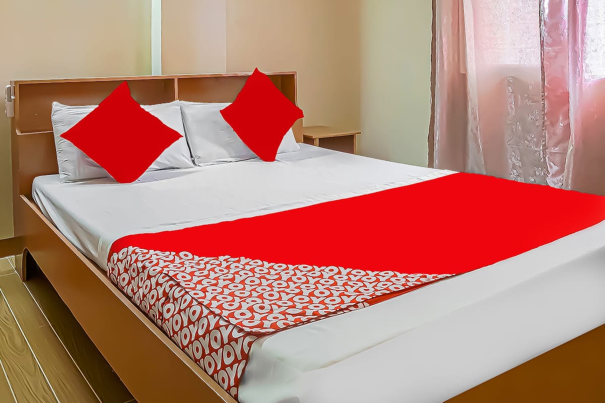 Un lit bien fait, avec une literie blanche et rouge, une tête de lit en bois et une petite table de chevet.