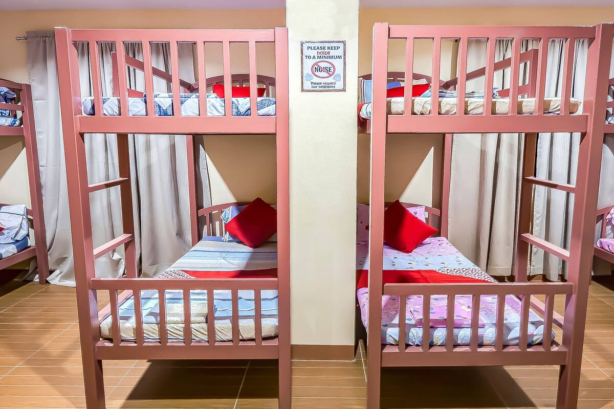 Une chambre avec des lits superposés, chacun étant équipé d’un rideau pour préserver l’intimité et d’une pancarte demandant aux occupants de faire le moins de bruit possible.