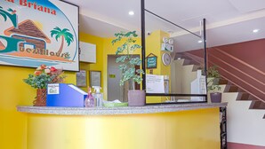 A reception desk with a tropical-themed poster, a clock, and a staircase in the background. - OYO 592 La Briana Guest House (Santa Fe)