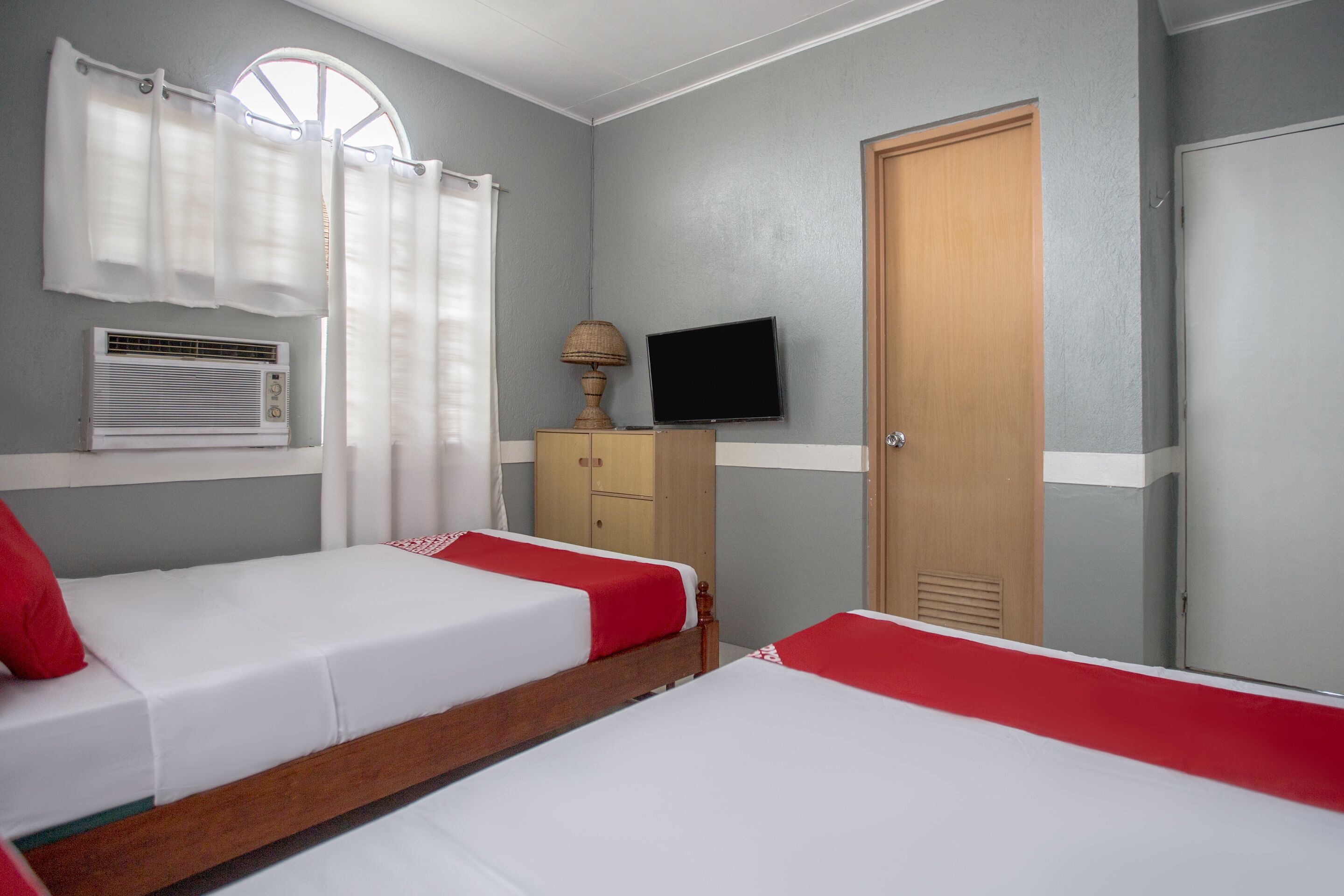 A hotel room with two beds, a television, a wardrobe, and a window with curtains.