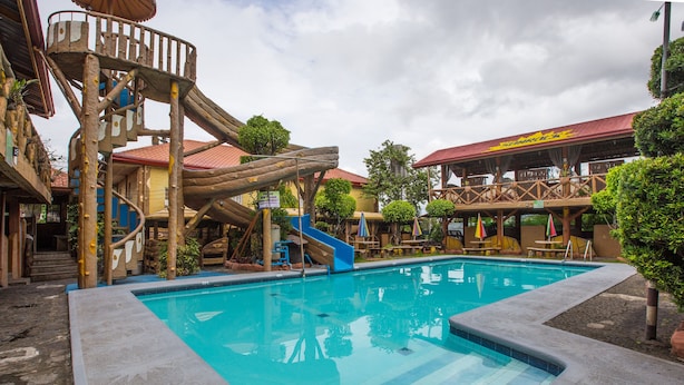 A swimming pool with a wooden slide and a jungle-themed play area. - OYO 588 Sunrock Resort (Antipolo)