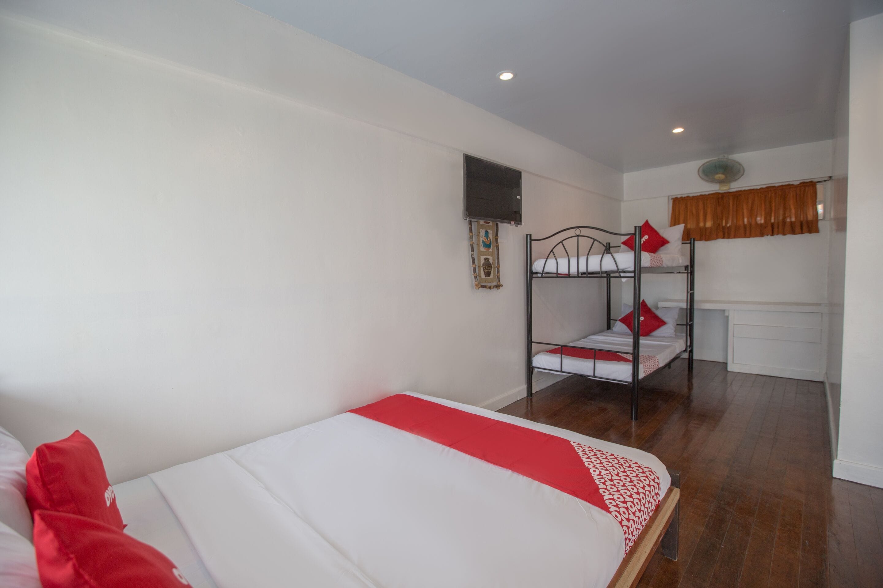 Une chambre avec un lit superposé, un lit simple, un petit bureau et une fenêtre avec des rideaux.