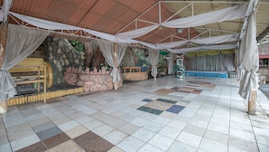 A spacious indoor area with a tiled floor, a stage with a blue backdrop, and a stone wall with plants. - OYO 588 Sunrock Resort (Antipolo)