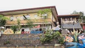 A building with a sign for Sun Rock Resort, featuring a stone wall with colorful murals and a balcony with a wooden railing. - OYO 588 Sunrock Resort (Antipolo)
