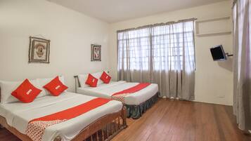 A hotel room with two beds, red pillows, a television, and a window with curtains.