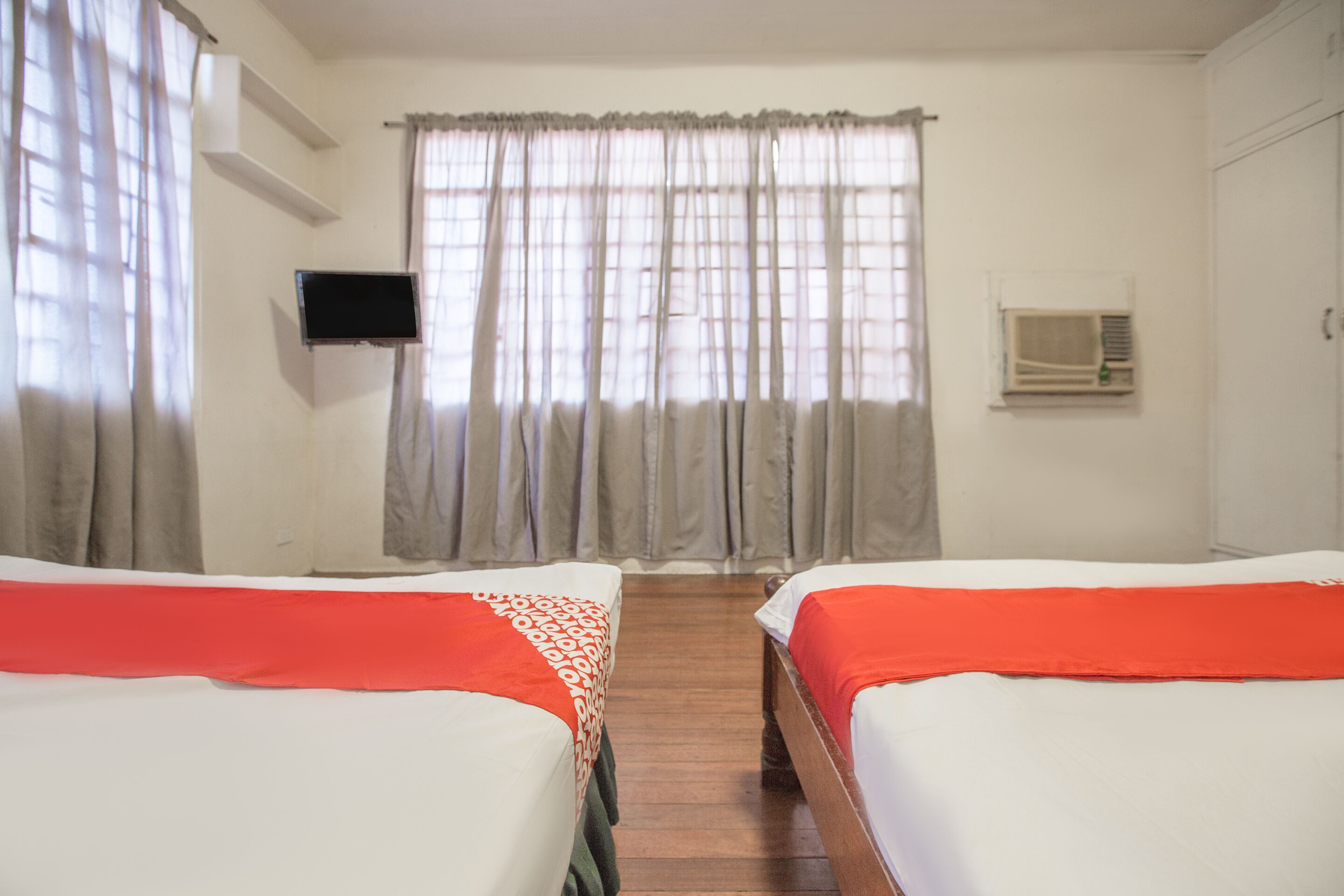 A hotel room with two beds, a television, and an air conditioning unit.