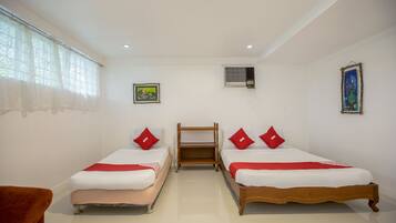 Habitación de hotel con dos camas individuales, una mesita de noche de madera, una pequeña mesa y una ventana con cortinas de gasa.