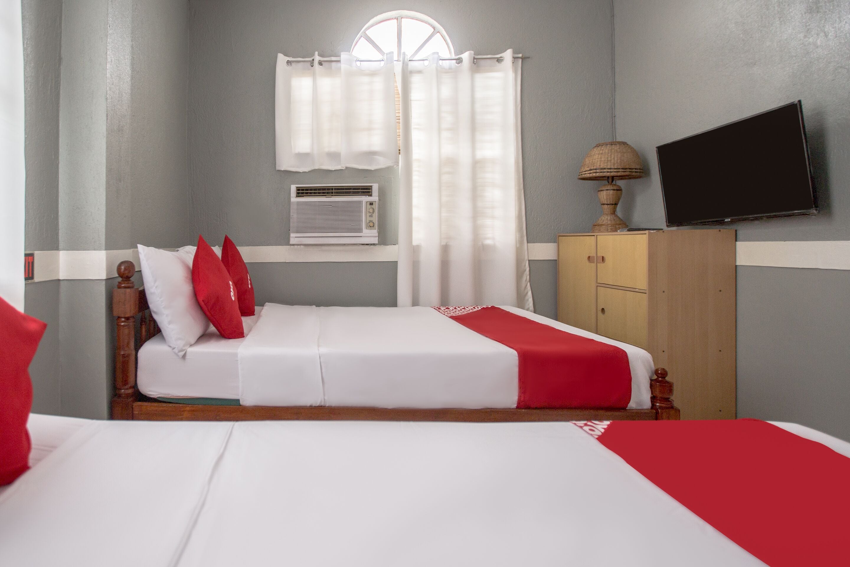 Una habitación de hotel con cama, televisor montado en la pared y ventana con cortinas.