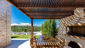 Eine Terrasse im Freien mit Holztisch und -stühlen, einem Grill und einer Steinmauer.