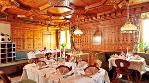 A restaurant with wooden paneling, round tables, and chandeliers. - Familiengut Ertlhof (Seeboden)