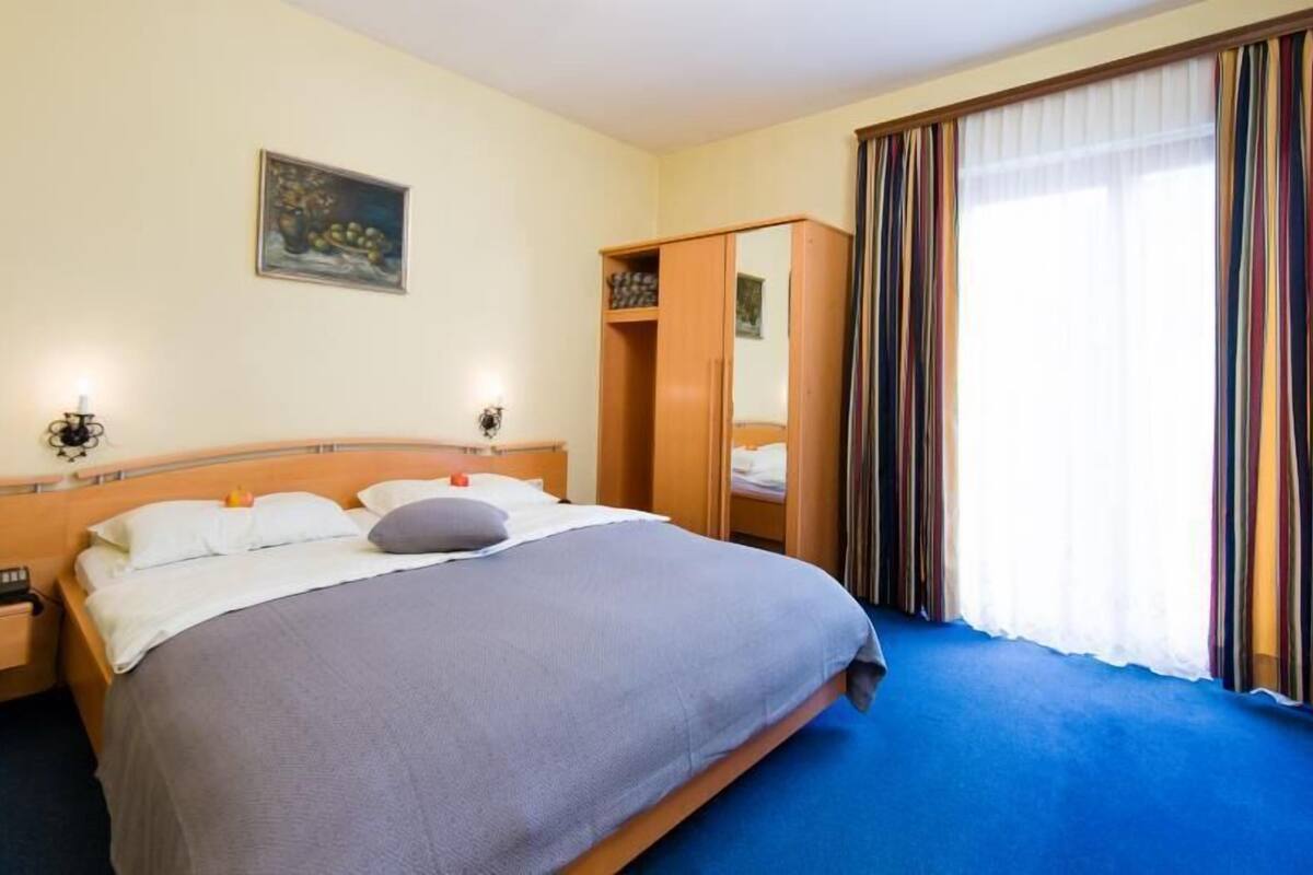A hotel room with a large bed, bedside tables, a wardrobe, and a painting on the wall.