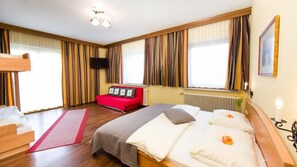 Una habitación de hotel con una cama, un sofá rojo, un televisor y cortinas.