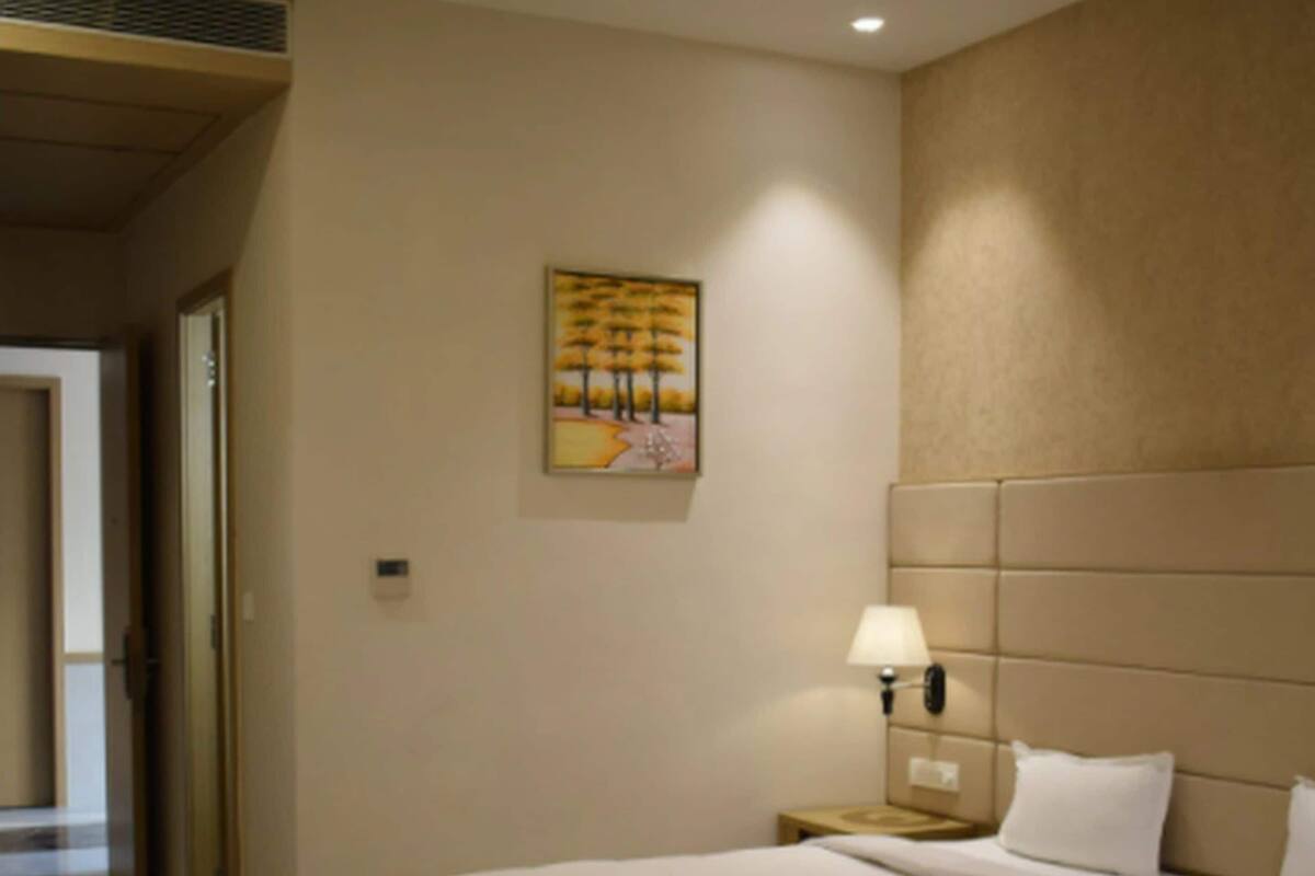 A hotel room with a bed, a nightstand, a lamp, and a painting on the wall.