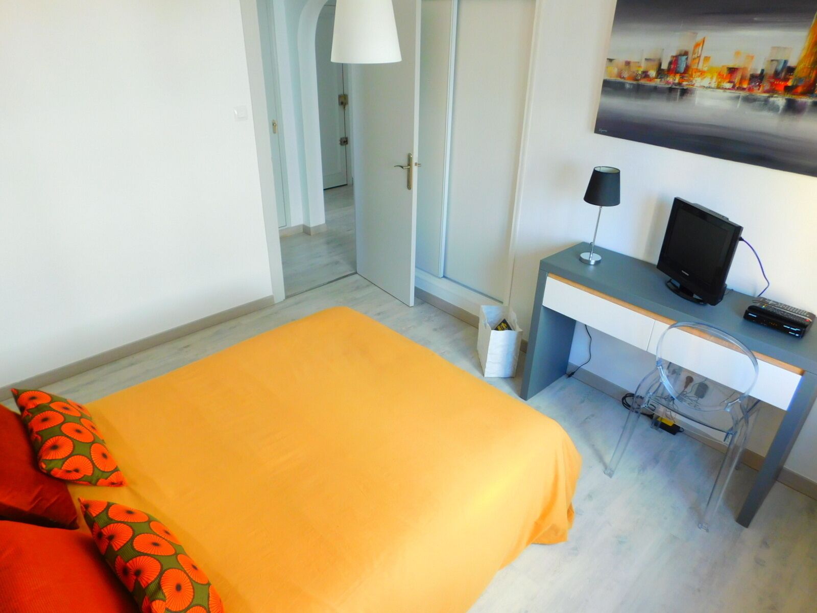 A hotel room with a bed, a desk with a computer, a chair, and a window with a cityscape view.
