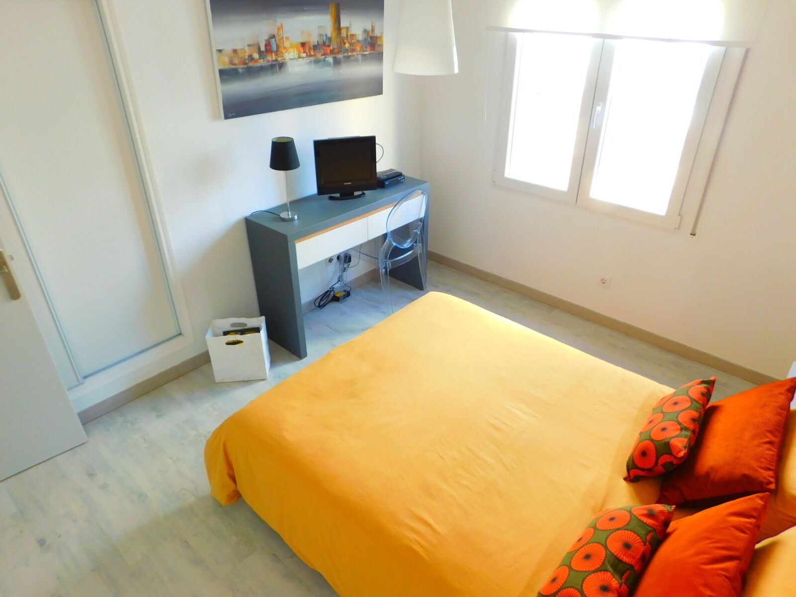 A bedroom with a bed, a desk with a computer, a chair, and a window.
