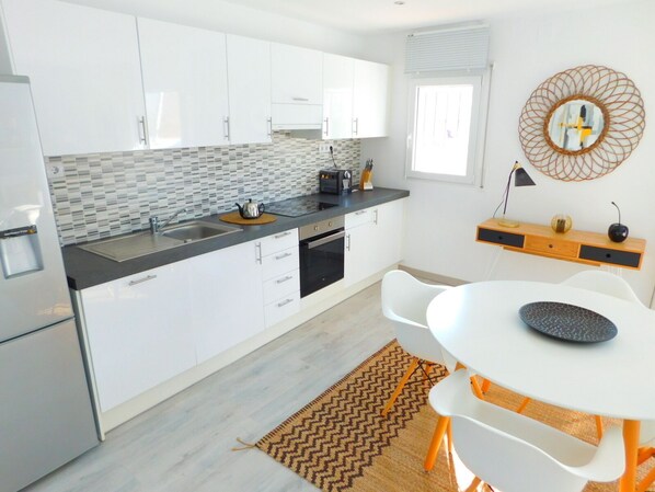 A modern kitchen with white cabinets, a black countertop, and a white dining table with orange legs.