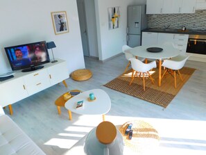 A modern living room with a TV, sofa, dining table, and kitchen area.
