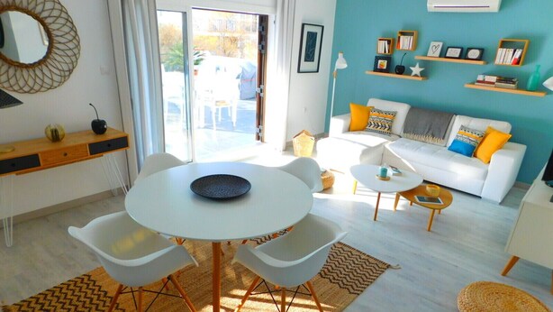 A modern living room with a white sofa, a round dining table, and a coffee table. There is a bookshelf with books and decorative items, and a large mirror on the wall. - Sea view apartment and private parking at 50 m. from the beach Salatar, Roses (Roses)