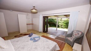 A bedroom with a bed, a chair, and a view of a garden through an open door. - Baleia Azul 26 (Zitundo)