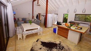 A spacious living area with a high ceiling, a dining table, a sofa, and a kitchen area with a countertop and appliances. - Baleia Azul 26 (Zitundo)