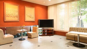 Una sala de estar moderna con un televisor de pantalla plana, sofás color beige, una mesita con un jarrón y obras de arte en las paredes.