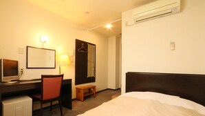 Habitación de hotel con cama, escritorio con ordenador, silla, espejo y aire acondicionado.