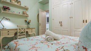 Ein Schlafzimmer mit einer blumigen Bettdecke, einem Schreibtisch mit Lampe und einem Kleiderschrank mit mehreren Türen.