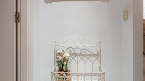 Eine weiße Tür mit einem Spiegel darüber, eine weiße Wand und eine weiße Metallbank mit einem Blumenstrauß.