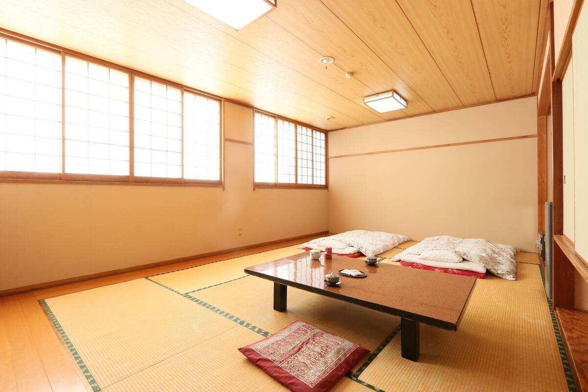 Ein Raum mit Tatami-Matten, einem niedrigen Tisch, Kissen und einem Futon.