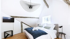 A bedroom with a bed, a TV, a wooden beam, a window, and a floor lamp. - Le Hoche Les Demoiselles in Versailles 1 minute from the Château de Versailles (Versailles)