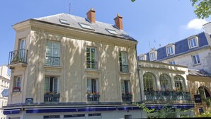 A historic building with multiple windows, a balcony with potted plants, and a sign indicating a business on the ground floor. - Le Hoche Les Demoiselles in Versailles 1 minute from the Château de Versailles (Versailles)
