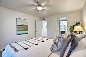 Een slaapkamer met een bed, een plafondventilator, een aan de muur hangend kunstwerk, een deur en een nachtkastje met een lamp.
