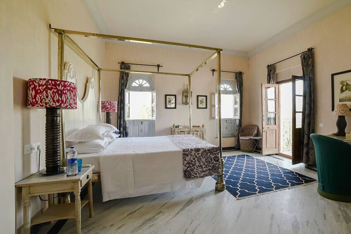 Una cama con dosel, un escritorio con lámpara y una silla en una habitación con un ventanal y vistas al exterior.