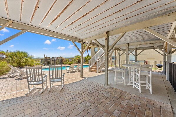 A covered outdoor area with a pool, lounge chairs, and a barbecue grill.